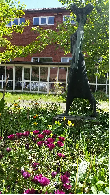 Blühende Blumen vor einer Skulptur im Schulgarten